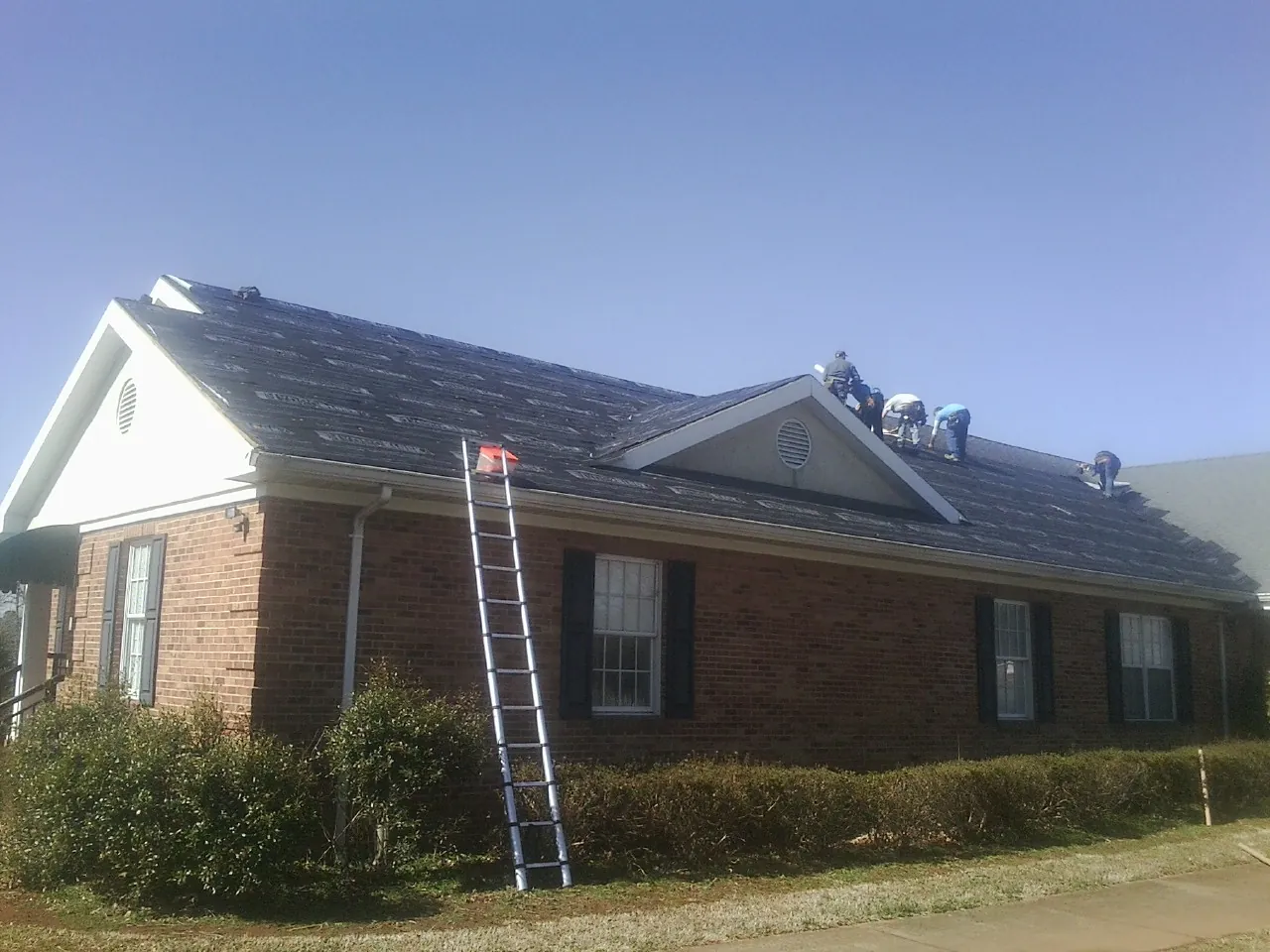 Crew tearing shingles off a brick ranch roof with a ladder set — Metal Roof Repair work by our crew in Briceville