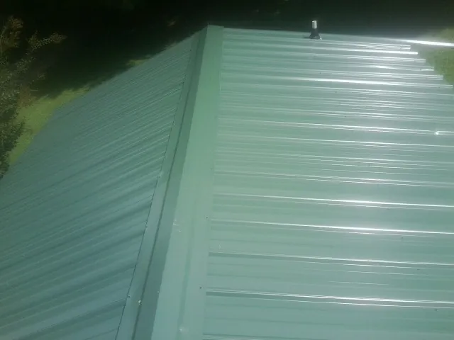 New green metal panels meeting at the ridge of a roof — Flat Roof Repair work by our crew in Briceville