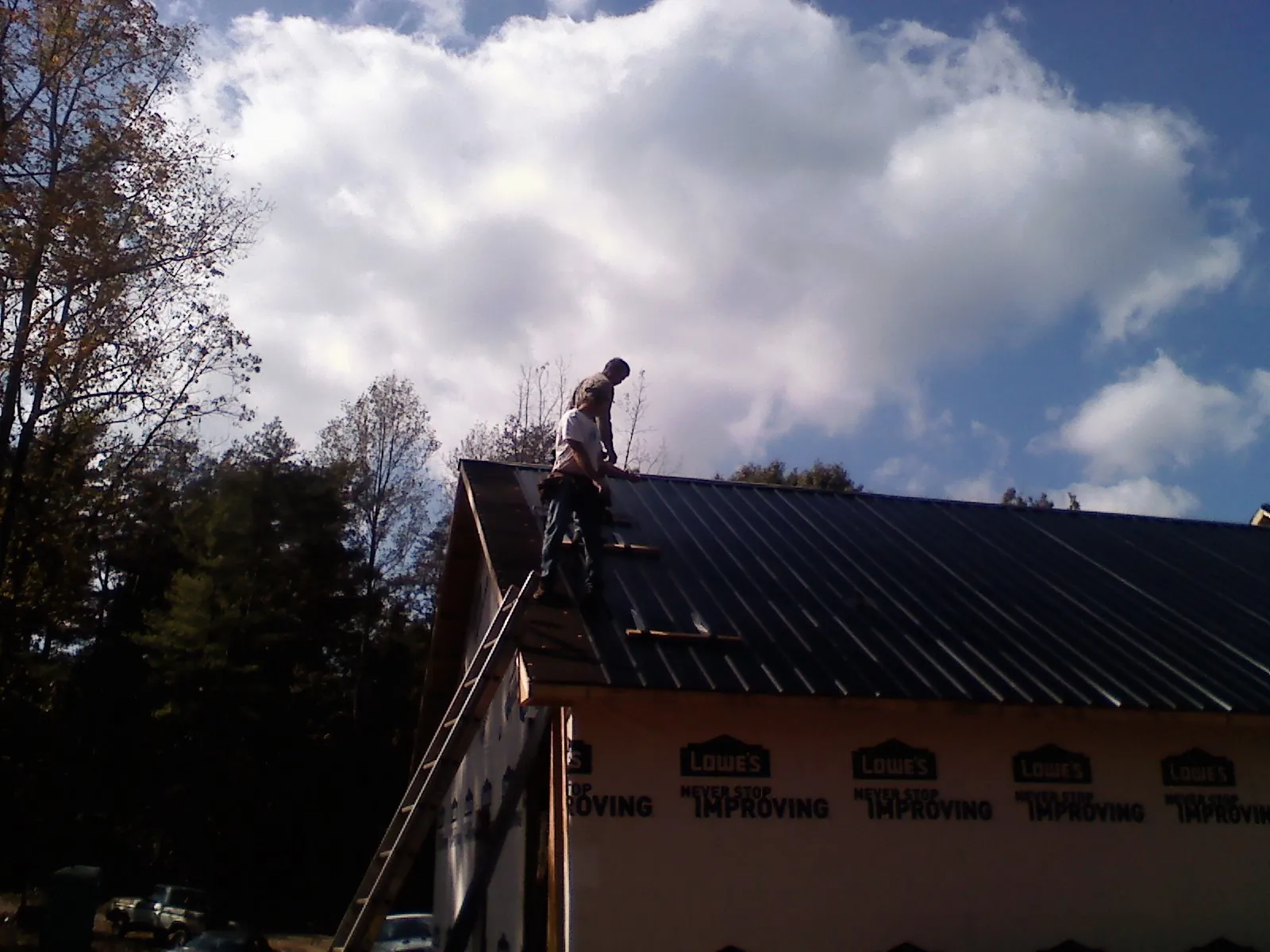 Roofer fastening dark metal panels high against a cloudy sky, from a Roof Inspection job in Briceville
