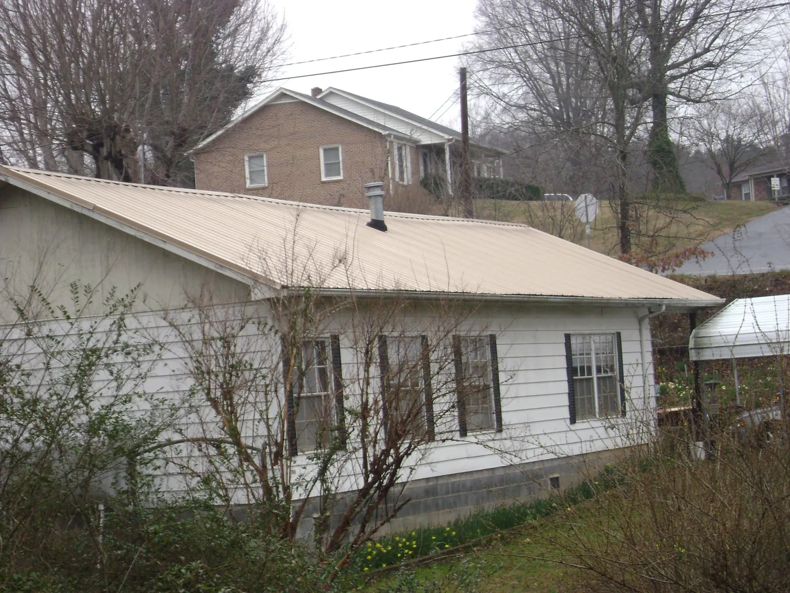 Tan metal roof on a white sided house set into a hillside — Commercial Roofing by Roofing Brothers in Briceville